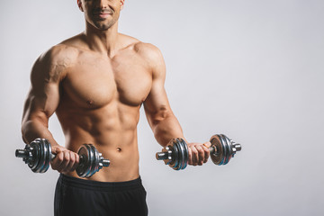 Muscular bodybuilder guy doing exercises with dumbbell over white background.
