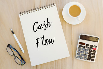 Top view of sunglasses,pen,calculator,a cup of coffee,and notebook written with Cash Flow on wooden background.Business,finance and banking concept.