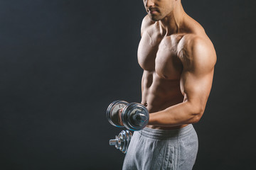 Muscular bodybuilder guy doing exercises with dumbbells over dark background. Close-up.