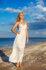 Fototapeta na wymiar beautiful young woman in white dress by the sea in the sun