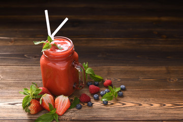 Mixed berry smoothie in glass with sliced berries on wooden background