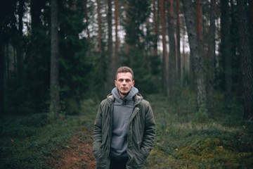  Caucasian young man in a forest in a green jacket.