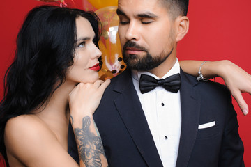 Naklejka premium Lovely female leaning on shoulder of attractive male and looking at him while standing near balloons on red background. Beautiful woman looking at handsome man