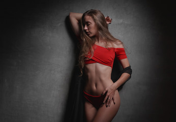Beautiful young woman in red bikini and black overall posing over gray wall background