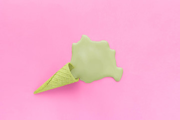 Sugar ice cream green waffle cone and green puddle of melted ice cream flowing out of it. Food and color concept. Layout on a pastel light purple background.