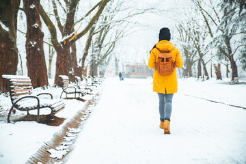 woman walking by snowed city park. view from behind. backpack.