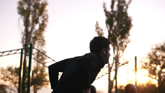 Fit man doing triceps dips on parallel bars at park exercising outdoors in the morning while listening to the music in earphones