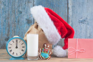 Obraz na płótnie Canvas Milk and cookies for Santa Claus and Santa's hat over wooden background.