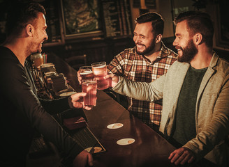 Old friends having fun and drinking draft beer at bar counter in pub.