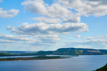River against the blue sky with clouds and forest.