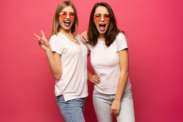 Two exited woman having fun and raising hands up. Standing on pink background. Lucky mood.