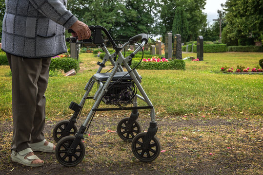 An old woman goes with her walking frame on the graveyard to be there with her survivors. Concept: mobility in old age or health