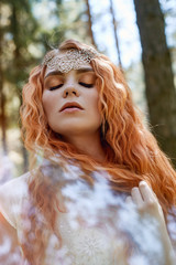 Fabulous portrait of a red-haired girl in nature with double exposure and glare. Beautiful redhead girl with long hair in the forest, mysterious look and big eyes, leaves and grass on her face