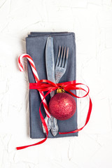 Christmas table place setting with knife, fork, red ball, candy cane and ribbon over white table with copyspace