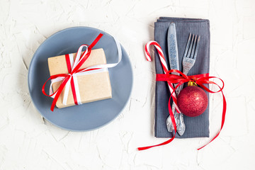 Christmas table place setting with napkin, fork, knife, ball, plate, candy canes and gift. holidays background.