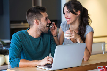 Beautiful young woman giving yogurt to her handsome boyfriend in the kitchen at home.