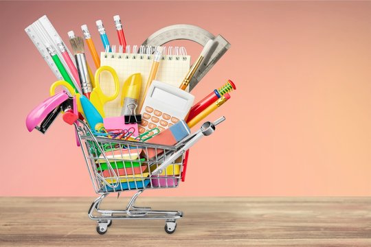 Variety office supplies in little shopping cart on wooden table