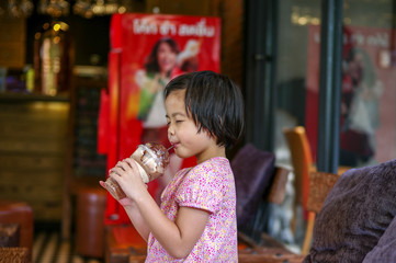 Portriat Asian little girl drinking blended ice chocolate with funny face. Happy girl enjoy eating soft drink with big smile and dimples on cheek at the cafe