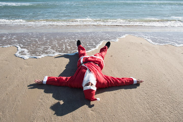 santa claus lying on the sand of a beach