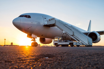 Fototapeta na wymiar White wide body passenger airplane with a boarding stairs at the airport apron in the evening sun