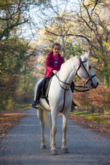 A girl rides a white horse in the forest