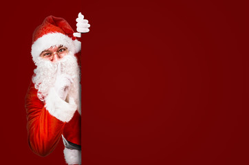 Santa Claus with finger on lips asking for silence with colorful advertisement board and copy space - 233037847