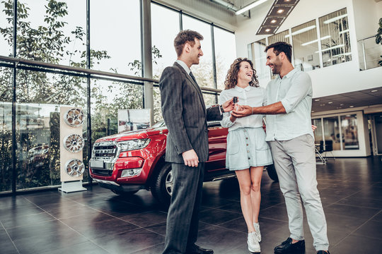 Car salesman is giving the key of the new car to the young attractive owners