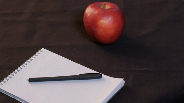 Close-up. A man raises his glasses from the table. A red apple lies next to a notepad and pen on a black cloth..