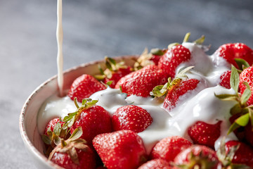 Closeup of ripe strawberries in a plate poured with fresh cream on a dark concrete background with copy space. Delicious vitamin dessert