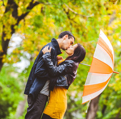 young couple in love with umbrella kissing in autumn season park