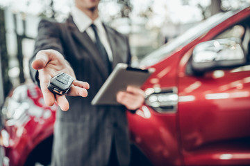Man in suit offering a car key to the observer, with a car in the background