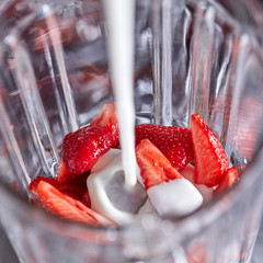 A blender with strawberry pieces is poured with fresh milk. Step-by-step preparation of milk drink....