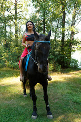 Beautiful brunette in a red suit of a dancer on horseback riding.