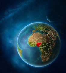 Planet Earth with highlighted Nigeria in space with Moon and Milky Way. Visible city lights and country borders.