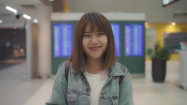 Slow motion - Happy Asian woman smiling to camera while staying at terminal in international airport, female tourist ready to travel on vacation. Lifestyle women happy holiday in the airport concept.