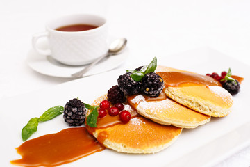 Pancakes with berries and maple syrup isolated in white.