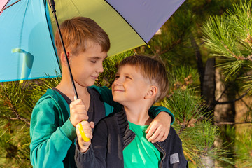 Two brothers stand in an embrace under a bright multi-colored umbrella and look at each other in a...