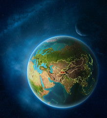 Planet Earth with highlighted Tajikistan in space with Moon and Milky Way. Visible city lights and country borders.