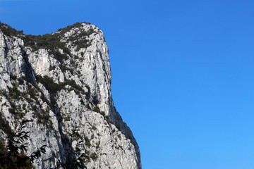 Vertical mountain cliff face against clear blue sky in summer