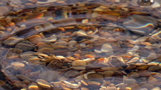 Powerful splash of seldom dripping in shallow pure water with pebble bottom close up in slow motion. Side view of amazing natural background with vibrant texture in sun shine. High speed camera shoot