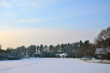 Snow-covered lake and houses on winter forest background. Christmas day.