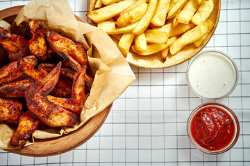 top view of delicious fried chicken wings, french fries and sauces on checkered tablecloth