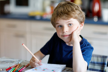 Happy smiling little kid boy at home making homework at the morning before the school starts. Little child doing excercise, indoors. Elementary school and education: Boy writing letters and numbers.