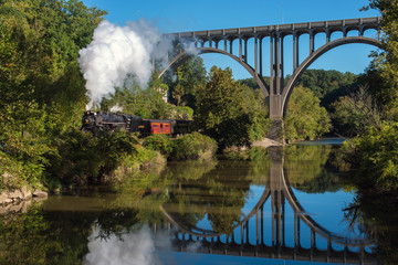 Steam locomotive crossing under a bridge over the river