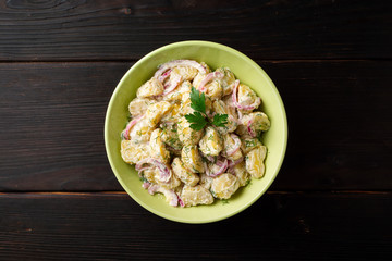 Potato salad with red onion and greens in bowl on dark wooden table. Top view. Copy space.