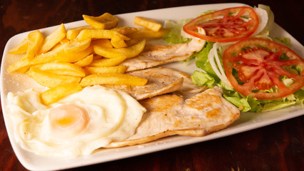 Fried egg with loin, french fries and tomato salad