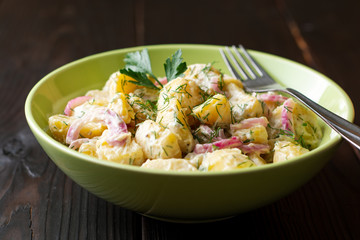 Potato salad with red onion and greens in bowl on dark wooden table. Selective focus.