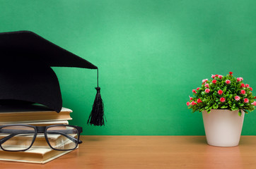 Stack of books, glasses and graduation cap on green school board background. Back to school.