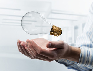 Concept of idea or energy as light bulb in male palms. Mixed med