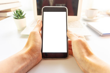 Desk in the office Hand is holding showing smartphone with blank mock up screen